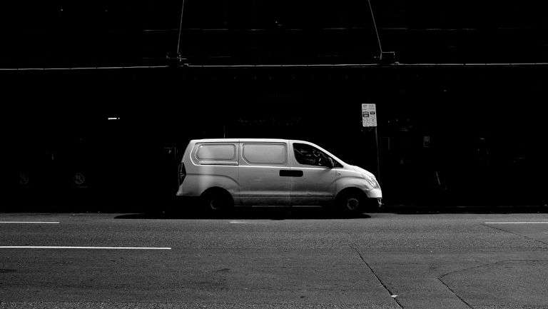 Black and white image of a van parked on a city street, capturing urban minimalism.